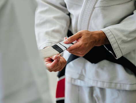 . Karate master tying a belt on a student in a dojo before practice. Closeup of a sensei help, prepare and assisting a beginner before exercise, workout and training in a sport club.