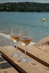 Glasses of cold rose wine from Provence served outdoor on wooden yacht pier with view on blue water and white sandy beach Plage de Pampelonne near Saint-Tropez, France