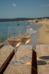 Glasses of cold rose wine from Provence served outdoor on wooden yacht pier with view on blue water and white sandy beach Plage de Pampelonne near Saint-Tropez, France