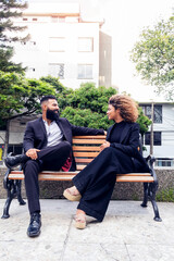 Coworkers chatting on park bench outdoors enjoying themselves happy, business partners chatting on park bench outdoors on sunny day