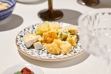 Cheese platter on white table with hard shadow. Cheeseboard with parmesan, gorgonzola, brie. Cheese appetizer in Italian menu. Aesthetic food composition with cheese assorted. Sunny day in tuscany.