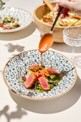 Classic french salad nicoise with tuna, vegetables and pouring sauce. Nicoise salad in ceramic plate on white table in sunny day. French cuisine in summer menu. Healthy salad with grilled tuna