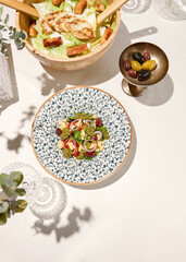 Traditional italian food - panzanella salad with tomatoes, onion rings and croutons. Panzanella salad on white table in summer menu. Composition with Tomato salad and glasses in sunny day.