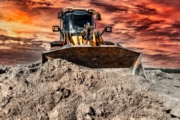 Powerful bulldozer or loader moves the earth at the construction site against the sky. An earthmoving machine is leveling the site. Construction heavy equipment for earthworks.