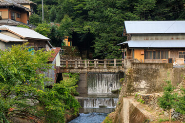 Fototapeta premium Small waterfall in river through village in Japanese countryside