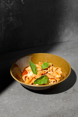 Italian pasta Pappardelle with tomato and mozzarella cheese on gray stone table. Tomato pasta pappardelle with cheese and basil. Veggie pasta with tomatoes on concrete background and shadow.