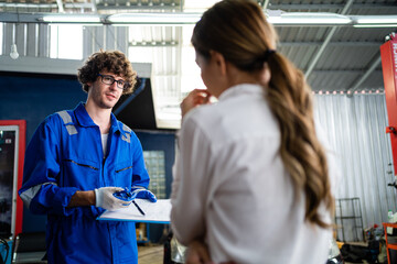 Obraz premium Car mechanic with a female customer. Car mechanic and female customer stand talking in the service center of the engine repair and inspection center. Mechanic service. Auto repair service concept.