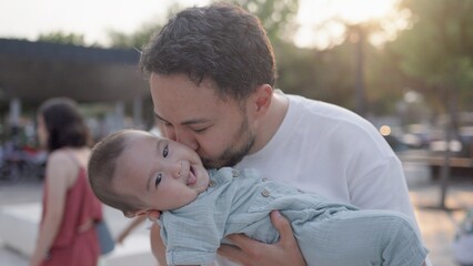 Happy father is holding cute baby and kisses while he is laughing