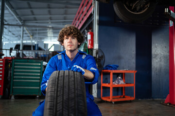 Auto repair service concept.  A portrait of a young Caucasian mechanic fixing a tire at a garage at the auto mechanic service station. The mechanic inspects the tire.