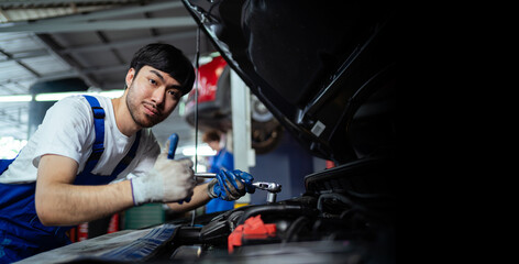 Fototapeta na wymiar Handsome young Asian mechanic checking his car with a wrench in the service center through the insurance system at the engine repair and inspection center.