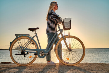 Naklejka premium Carefree woman with bike riding on sand beach having fun, on the seaside promenade on a summer day. 