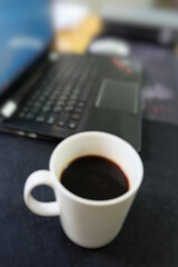 Blurred picture of a cup of coffee and a laptop.