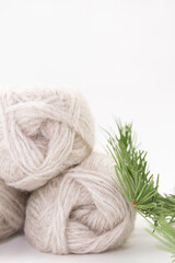 Balls of gray yarn and a spruce branch on a white background. Knitting, sewing, needlework, hobby, leisure. Copy space