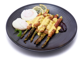 baked aspargus covered with bacon on a black ceramic plate isolated on white background