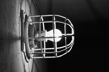 Glowing incandescent lamp. Old electric light bulb with a metal grate on the wall
