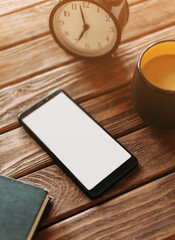 Phone with an empty place for a mockup on the screen on a wooden table near a cup of coffee and clock.