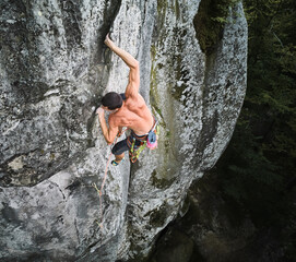 Young man climber climbing difficult route on high boulder with rope. Fearless rock climber...