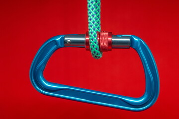 Aluminum climbing D-shaped carabiner hangs on a rope (red background)