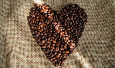 Roasted coffee beans laid out in heart shape on burlap background. Love coffee concept. Advertising cafe mockup.