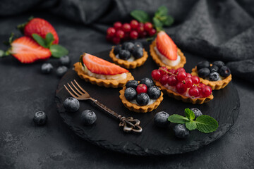 Obraz na płótnie Canvas Delicious tartlets with fruit and cream mascaropne on black board