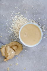 Pure sesame tahini with sesame seeds on mottled grey with copy space