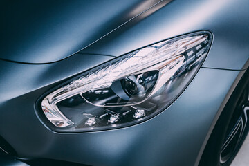Close-up detailed view of the headlights of a luxury car in the garage. Halogen and xenon headlamp lighting and auto tuning systems - obrazy, fototapety, plakaty