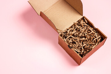 Open brown box with brown shredded paper on pink background. Paper gift box with decorative straws...