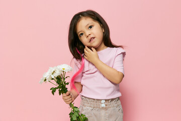 a cute little preschool girl stands on a pink background in a pink T-shirt and shows a bouquet of white daisies, actively moving her hands, smiling happily. The theme of children's delight