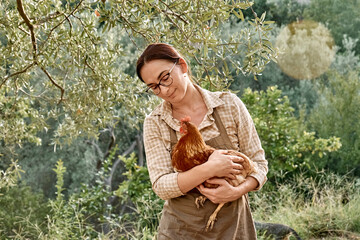 Woman holding brown hen in her hands in the farm. Free-grazing domestic hen on a traditional free...
