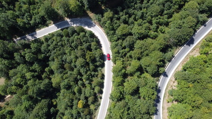 Drohnenaufnahme/Luftaufnahme von oben von gekurvtem Weg im Wald mit isoliertem rotem Auto im...
