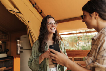 Cheerful young caucasian girls in mood hold smartphone enjoying pastime in countryside. Brunettes wear casual clothes spring. Lifestyle concept