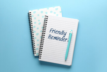 Notebooks with text FRIENDLY REMINDER and pen on blue background