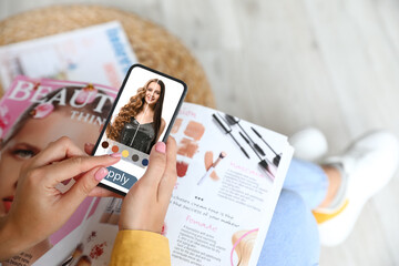 Young woman with cell phone using hair style application at home