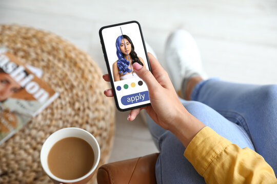 Young woman with mobile phone using hair style application at home