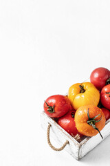 Fresh colorful tomatoes (red, yellow, orange) in a white rustic box on white background with copy space