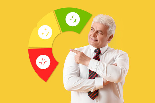 Mature businessman pointing at different emoticons on yellow background - Powered by Adobe