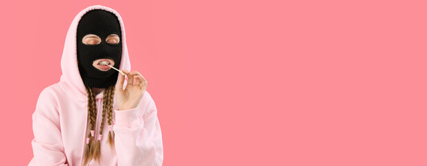 Young woman in balaclava and hoodie chewing gum on pink background with space for text
