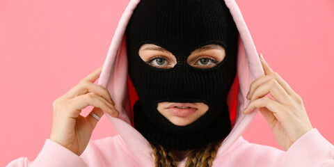 Young woman in balaclava and hoodie on pink background