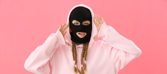 Young woman in balaclava and hoodie on pink background
