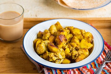 Cauliflower with potatoes and spices in a white plate on a light concrete background. Indian food. Vegan food.