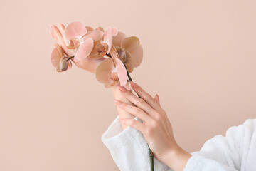 Young woman with beautiful orchid flowers on beige background - obrazy, fototapety, plakaty