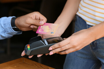 Man paying with credit card via payment terminal at table in cafe, closeup