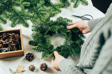Woman making a christmas fir wreath. Christmas decorating for home interior.