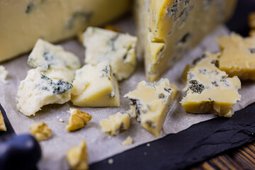 Tasty blue cheese served with grape and green on a wooden background. Dorblu cheese pieces