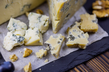 Tasty blue cheese served with grape and green on a wooden background. Dorblu cheese pieces