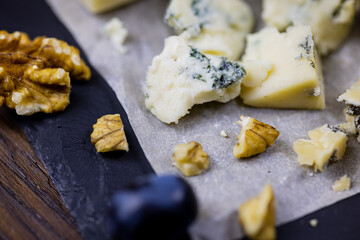 Tasty blue cheese served with grape and green on a wooden background. Dorblu cheese pieces