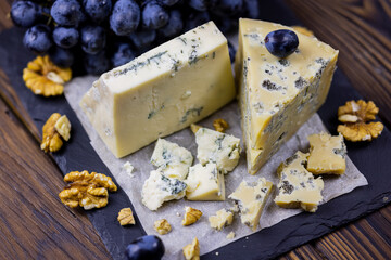 Tasty blue cheese served with grape and green on a wooden background. Dorblu cheese pieces