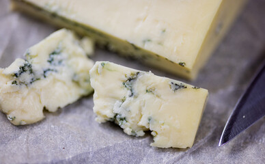 Tasty blue cheese served with grape and green on a wooden background. Dorblu cheese pieces