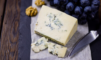 Tasty blue cheese served with grape and green on a wooden background. Dorblu cheese pieces