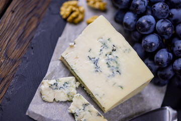 Tasty blue cheese served with grape and green on a wooden background. Dorblu cheese pieces